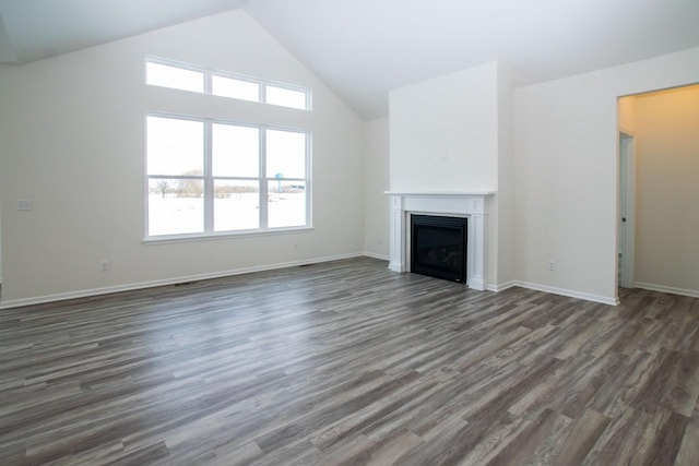 unfurnished living room featuring high vaulted ceiling, baseboards, dark wood-type flooring, and a glass covered fireplace