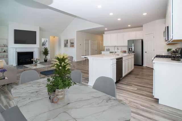 dining space featuring light wood-type flooring, a fireplace, vaulted ceiling, and recessed lighting