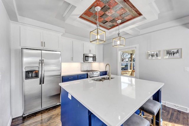 kitchen with dark wood finished floors, stainless steel appliances, a raised ceiling, a sink, and blue cabinets