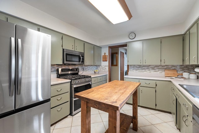 kitchen with green cabinetry, light tile patterned flooring, stainless steel appliances, light countertops, and backsplash