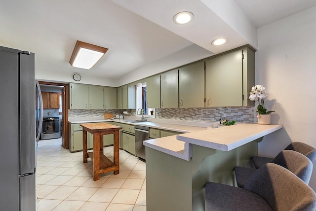 kitchen featuring green cabinets, a peninsula, light tile patterned flooring, stainless steel appliances, and a sink