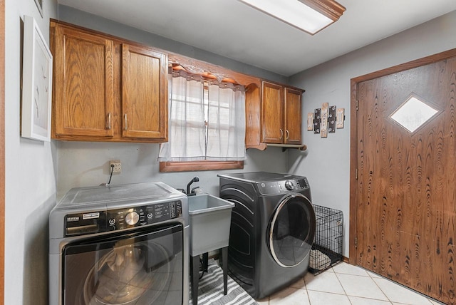 clothes washing area with cabinet space, light tile patterned floors, washing machine and dryer, and a sink