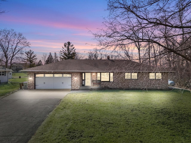 view of front of house featuring driveway, roof with shingles, a garage, a lawn, and brick siding