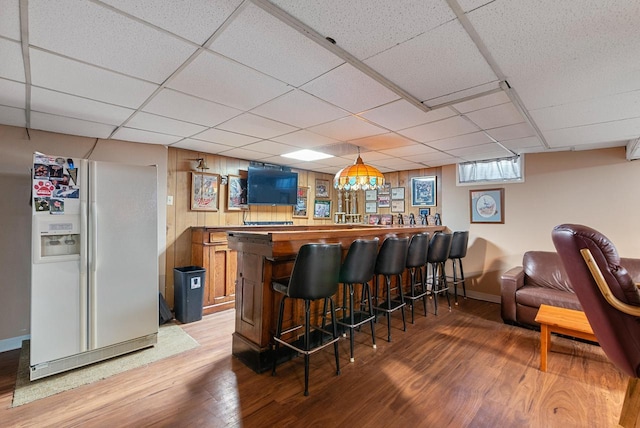 bar featuring a paneled ceiling, light wood-style floors, white refrigerator with ice dispenser, and a bar