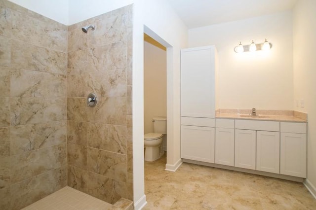 bathroom with baseboards, a tile shower, vanity, and toilet