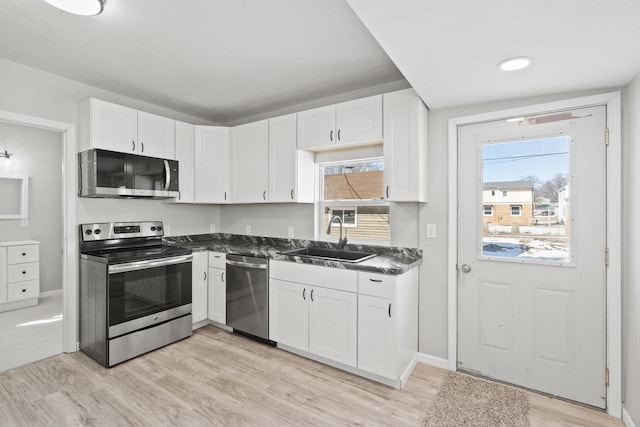 kitchen featuring white cabinets, dark countertops, stainless steel appliances, and a sink