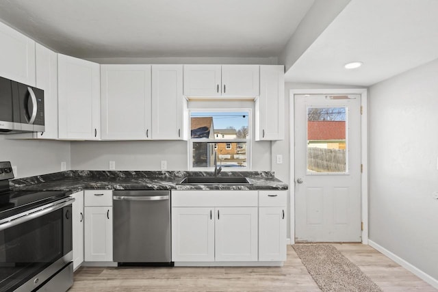 kitchen with dark countertops, appliances with stainless steel finishes, light wood-style floors, white cabinetry, and a sink