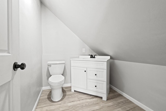 bathroom with baseboards, toilet, lofted ceiling, wood finished floors, and vanity