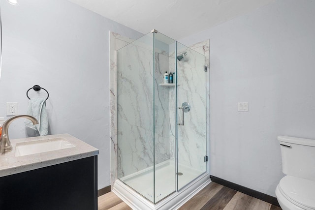 bathroom with a marble finish shower, toilet, vanity, wood finished floors, and baseboards