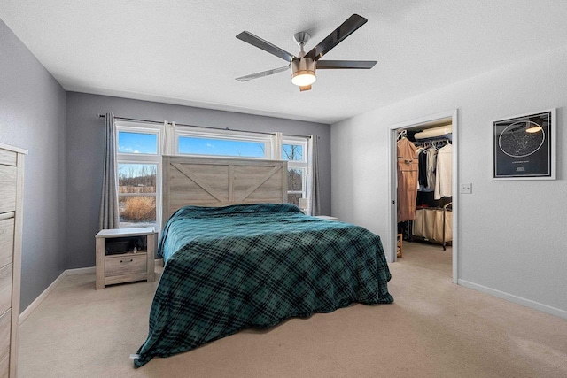 bedroom featuring light carpet, a walk in closet, a ceiling fan, and baseboards