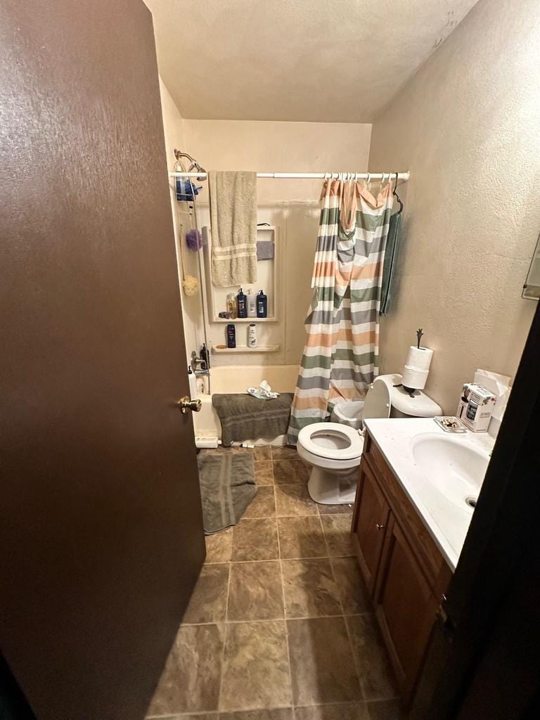 bathroom with a textured wall, vanity, toilet, and shower / bath combo with shower curtain