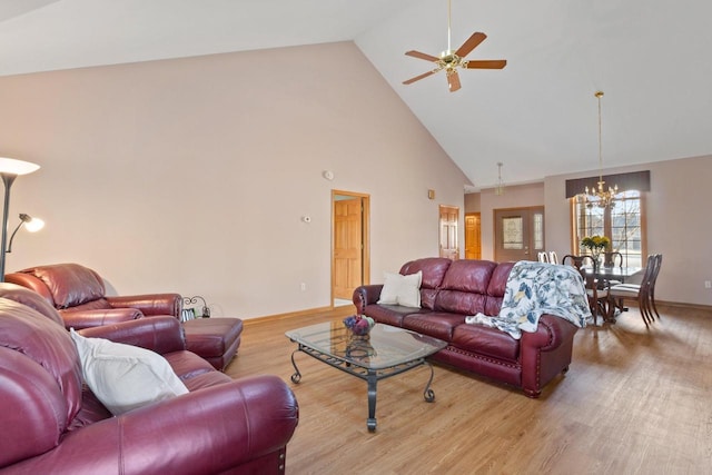 living area with ceiling fan with notable chandelier, wood finished floors, baseboards, and high vaulted ceiling