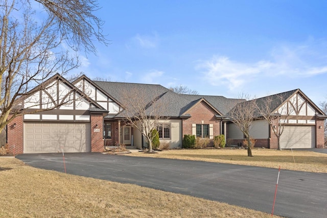 tudor-style house with aphalt driveway, an attached garage, a shingled roof, and brick siding