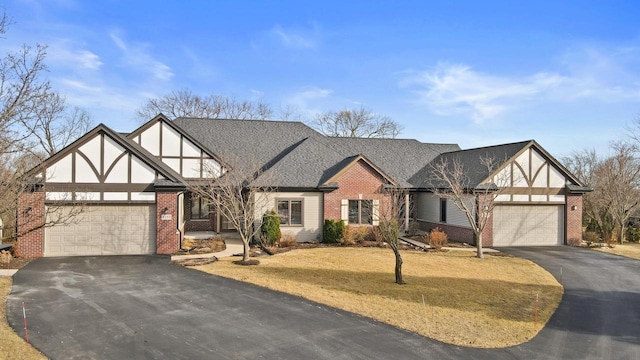 english style home with a front yard, driveway, a shingled roof, a garage, and brick siding