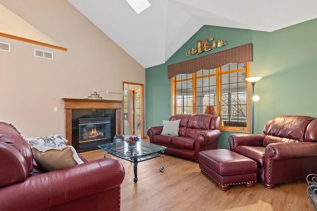 living room with visible vents, a fireplace, a skylight, wood finished floors, and high vaulted ceiling