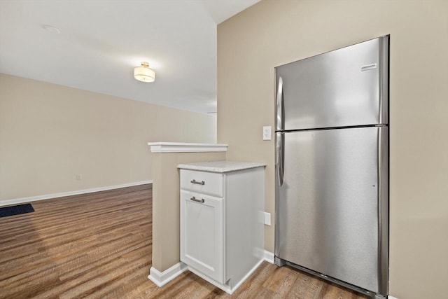 kitchen with freestanding refrigerator, baseboards, white cabinets, and light wood finished floors