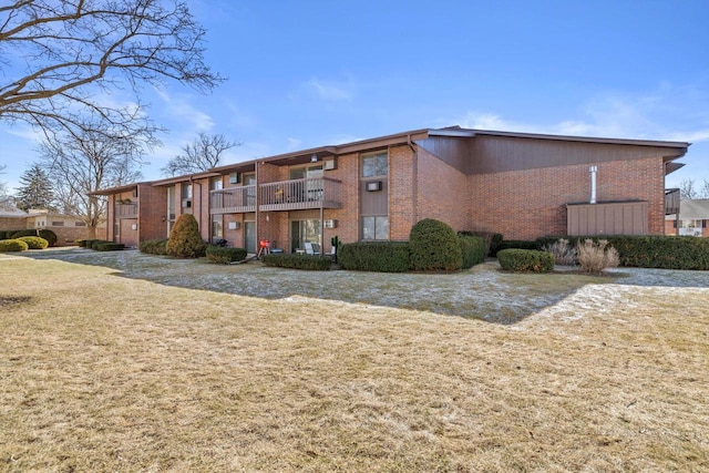 view of front of property with brick siding, a balcony, and a front lawn