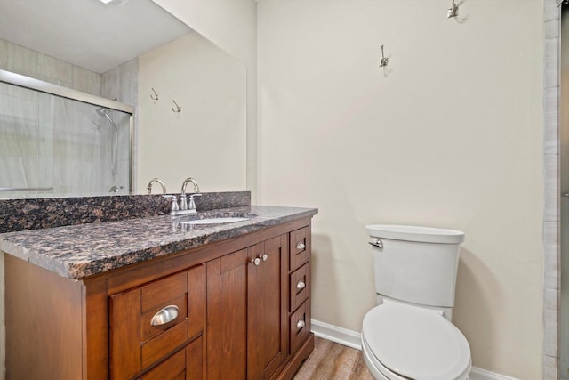 bathroom featuring toilet, a shower with shower door, wood finished floors, vanity, and baseboards