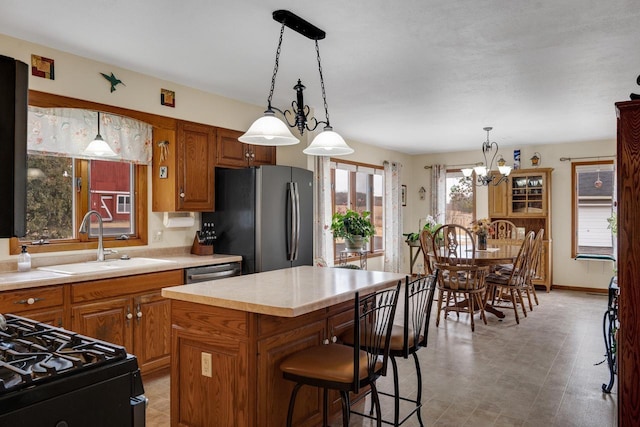 kitchen featuring brown cabinetry, a kitchen island, appliances with stainless steel finishes, light countertops, and a sink