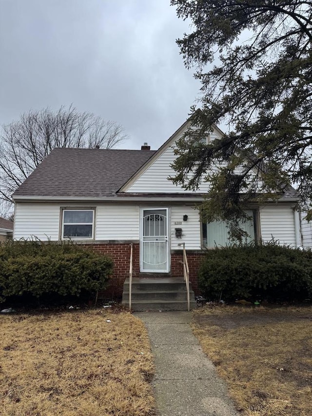 view of front of house featuring entry steps, roof with shingles, brick siding, and a chimney