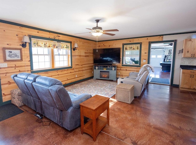 living room with a warm lit fireplace, ceiling fan, and wood walls