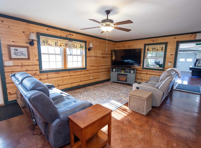 living room featuring ceiling fan, a lit fireplace, and wood walls