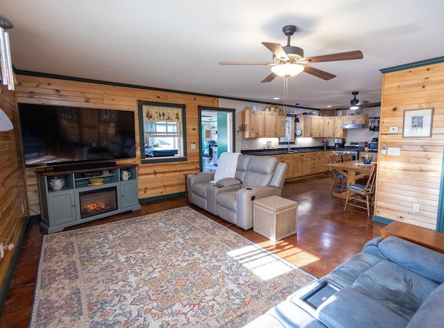 living room featuring a ceiling fan, concrete flooring, wood walls, and a lit fireplace