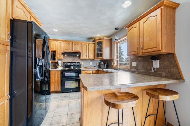 kitchen with glass insert cabinets, a peninsula, under cabinet range hood, black appliances, and a sink