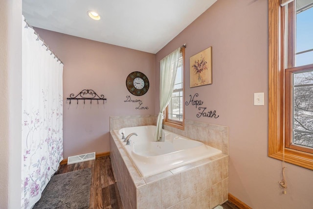 bathroom with wood finished floors, a garden tub, visible vents, and baseboards