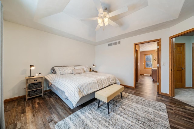 bedroom with a tray ceiling, dark wood-style flooring, visible vents, and baseboards