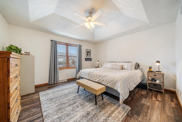 bedroom featuring a tray ceiling, dark wood-style flooring, and baseboards