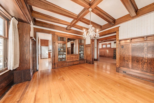 empty room featuring beamed ceiling, coffered ceiling, wood-type flooring, and a wealth of natural light