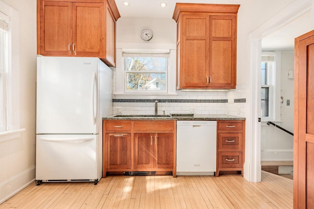 kitchen featuring white appliances, a sink, backsplash, and dark stone countertops