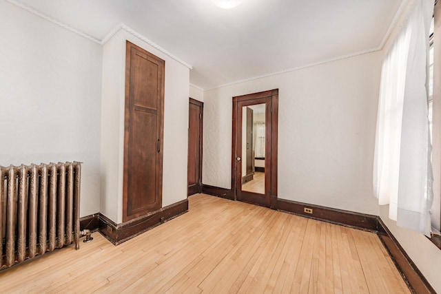 unfurnished room featuring baseboards, light wood finished floors, ornamental molding, and radiator