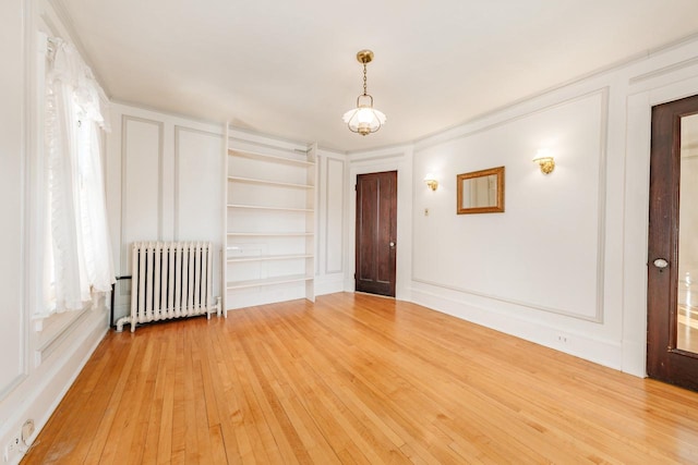 spare room with built in shelves, a decorative wall, light wood-style floors, and radiator