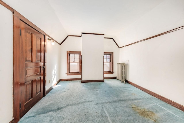 interior space with baseboards, light colored carpet, radiator, lofted ceiling, and crown molding