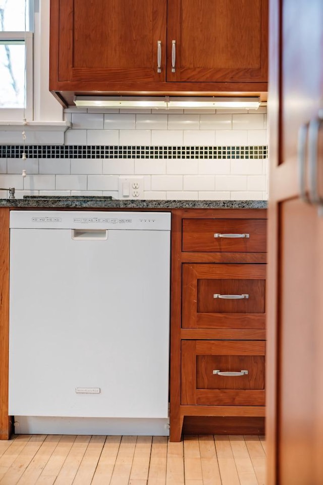 kitchen with white dishwasher, decorative backsplash, brown cabinetry, and dark stone countertops