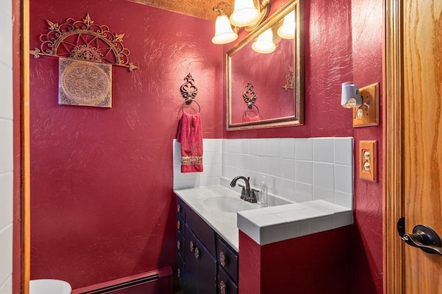 bathroom with vanity, a baseboard heating unit, backsplash, and a textured wall