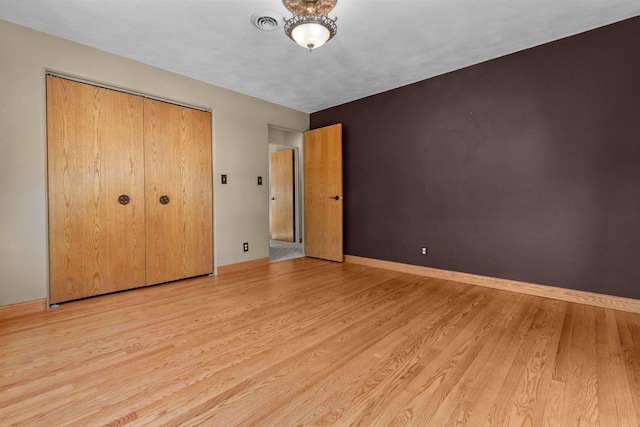 unfurnished bedroom with a closet, wood finished floors, visible vents, and baseboards