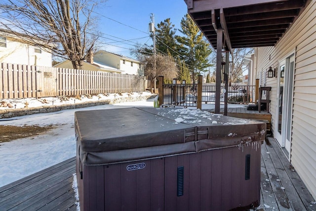 snow covered deck featuring a hot tub and fence