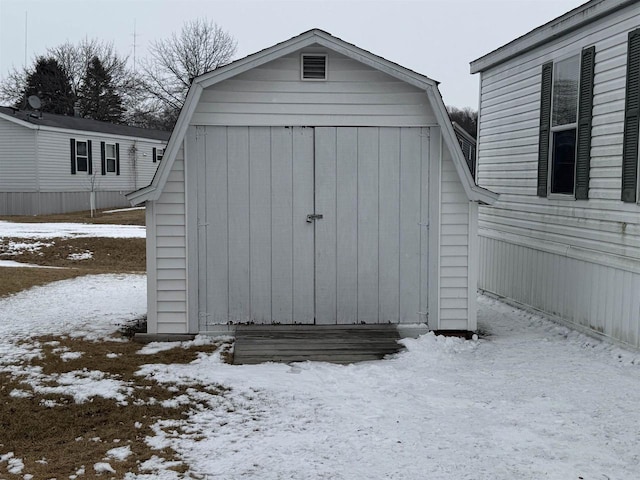 snow covered structure featuring an outbuilding and a storage shed