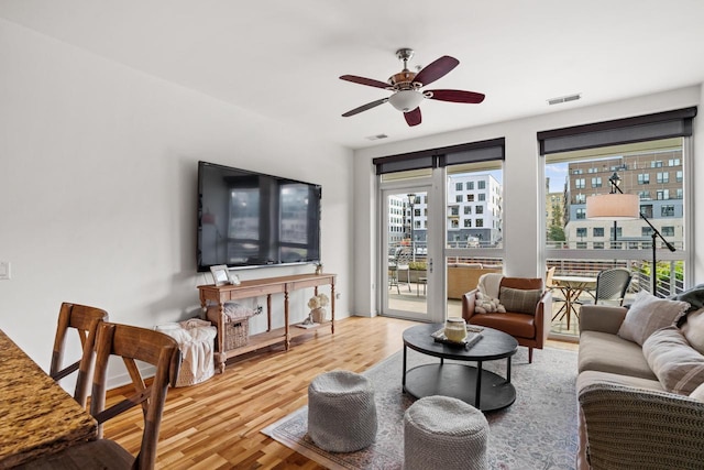 living room with a ceiling fan, visible vents, and wood finished floors