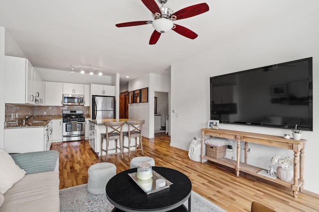 living area with light wood-type flooring, a ceiling fan, and baseboards