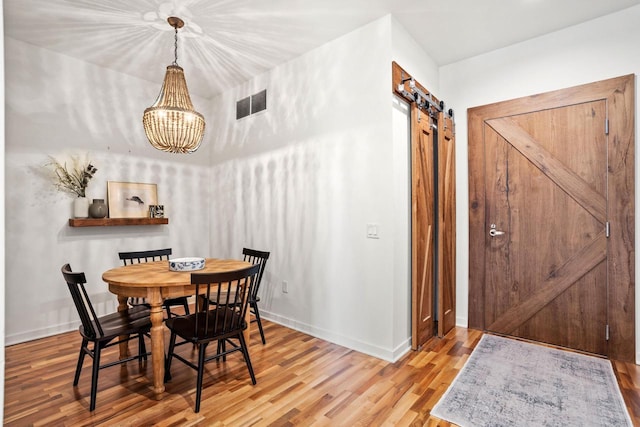 dining space with a barn door, baseboards, visible vents, wood finished floors, and an inviting chandelier