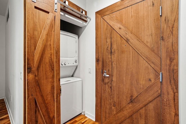 laundry area with stacked washer and dryer, visible vents, baseboards, and a barn door