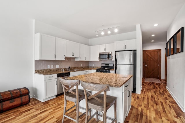 kitchen with stainless steel appliances, white cabinetry, light wood-style flooring, and tasteful backsplash