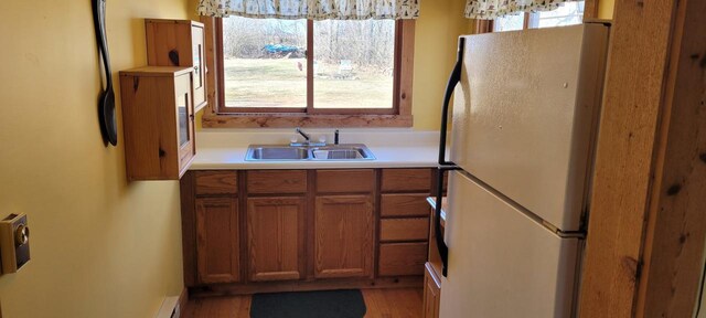 kitchen with brown cabinets, light countertops, light wood-style flooring, freestanding refrigerator, and a sink