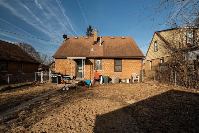 rear view of house featuring brick siding, central air condition unit, a chimney, and a fenced backyard