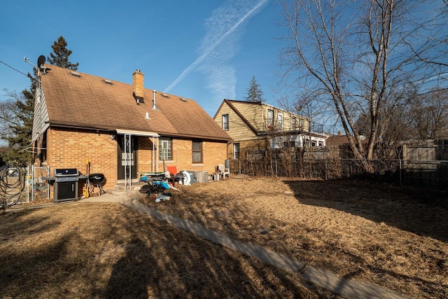 rear view of house featuring a patio, brick siding, a fenced backyard, and a chimney