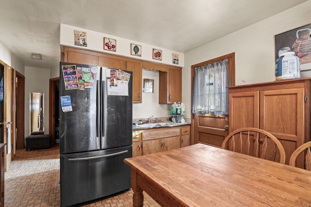 kitchen featuring brown cabinetry, butcher block counters, freestanding refrigerator, and a sink